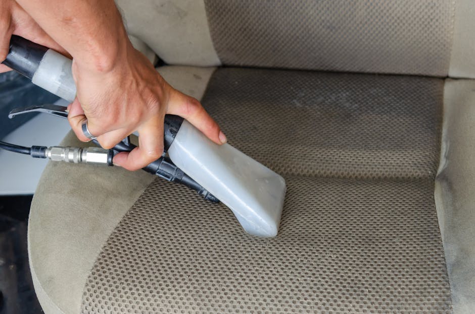A woman with curly brown hair wearing a green t-shirt is performing surface cleaning on a large white sofa in a well-lit room. She is carefully smoothening and wiping the fabric of the sofa, which app